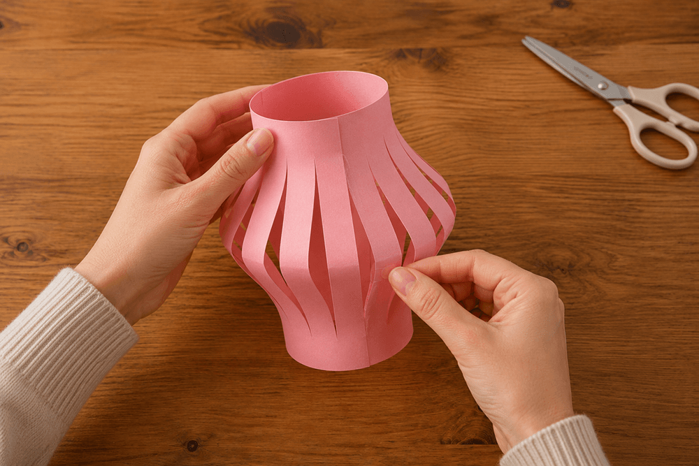 Gluing a white vellum paper layer inside pink cut paper to soften the glow of a handmade paper lantern