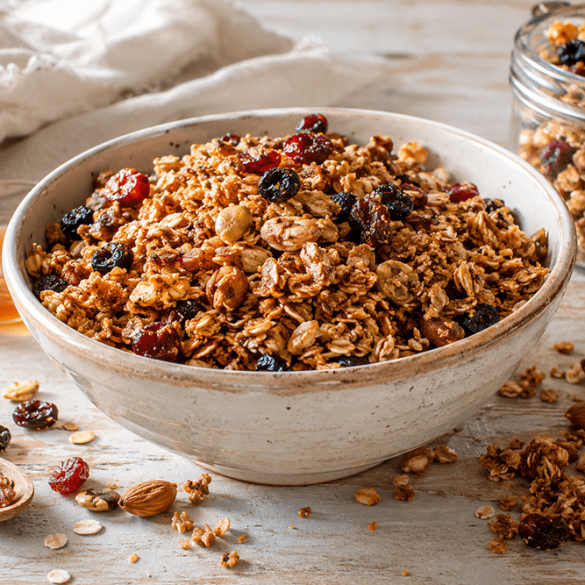 Homemade pantry staples granola in a ceramic bowl with oats, nuts, dried cranberries, raisins, and honey on a rustic breakfast table